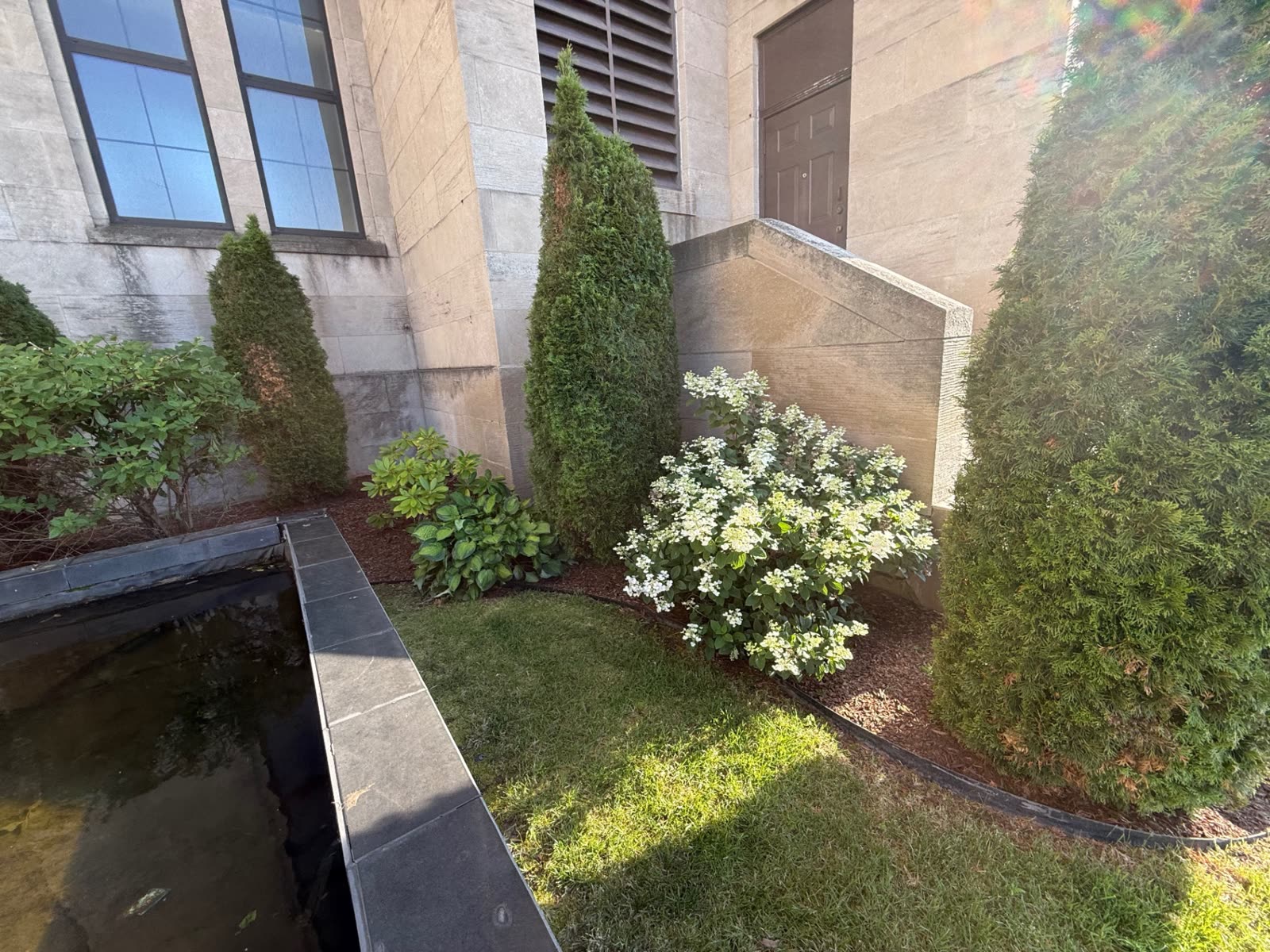 Foundation plantings and lawn border beside a limestone building